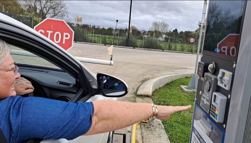 Photo showing a woman leaning out her car window to use the touch screen to sign in on the weighbridge. There is a help button for assistance.